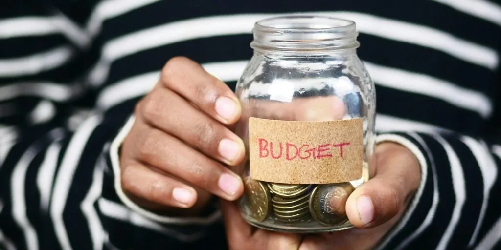 Hands holding a coin jar labeled BUDGET – Zidika Consulting Kenya